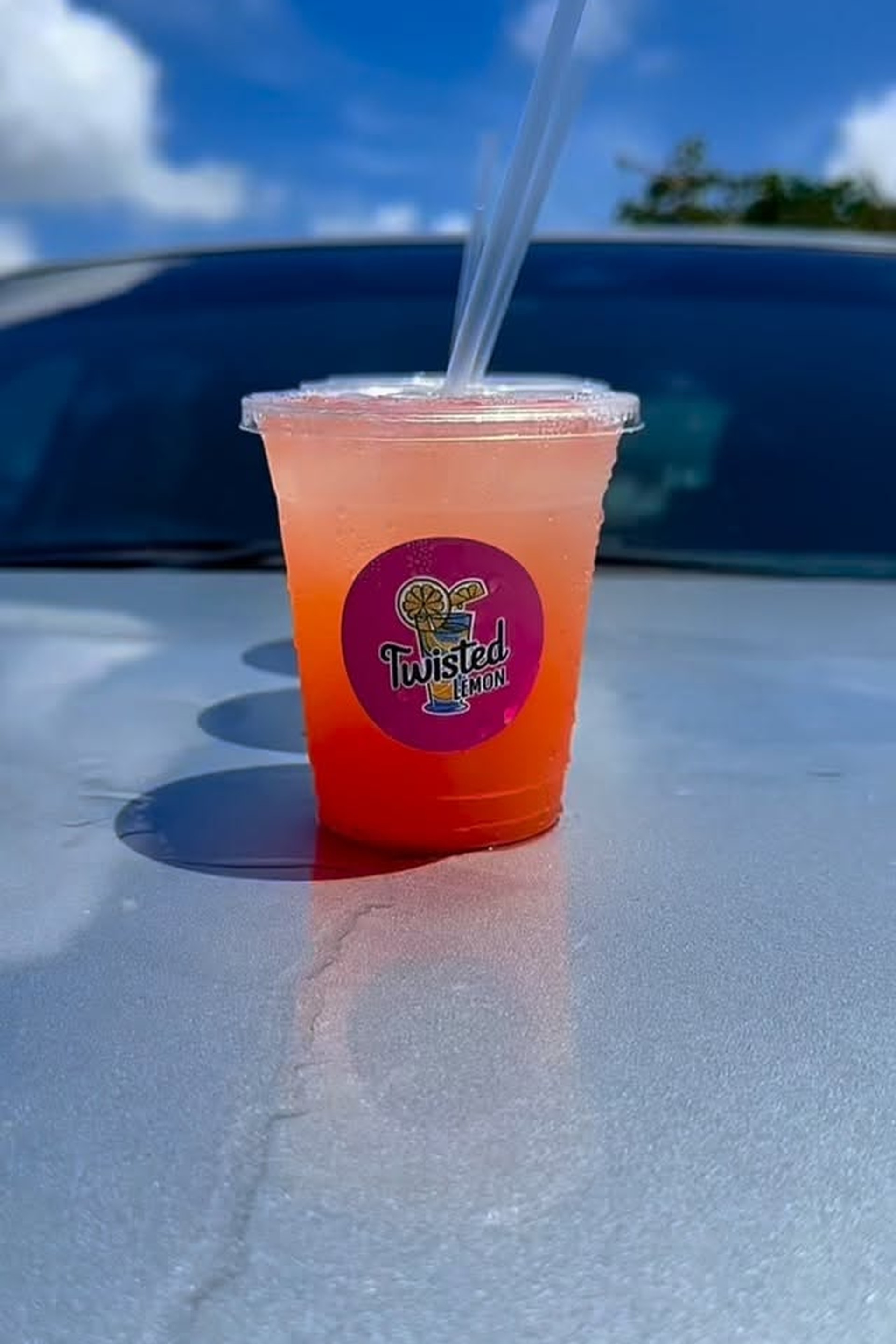 A person holding a cold Twisted Lemon cup amidst a spread of lemonade, desserts, and beer.